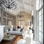 Una mesa, sillones blancos y un sofá con almohadas blancas y grises.