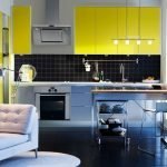 La combinación de un delantal negro y muebles amarillos.